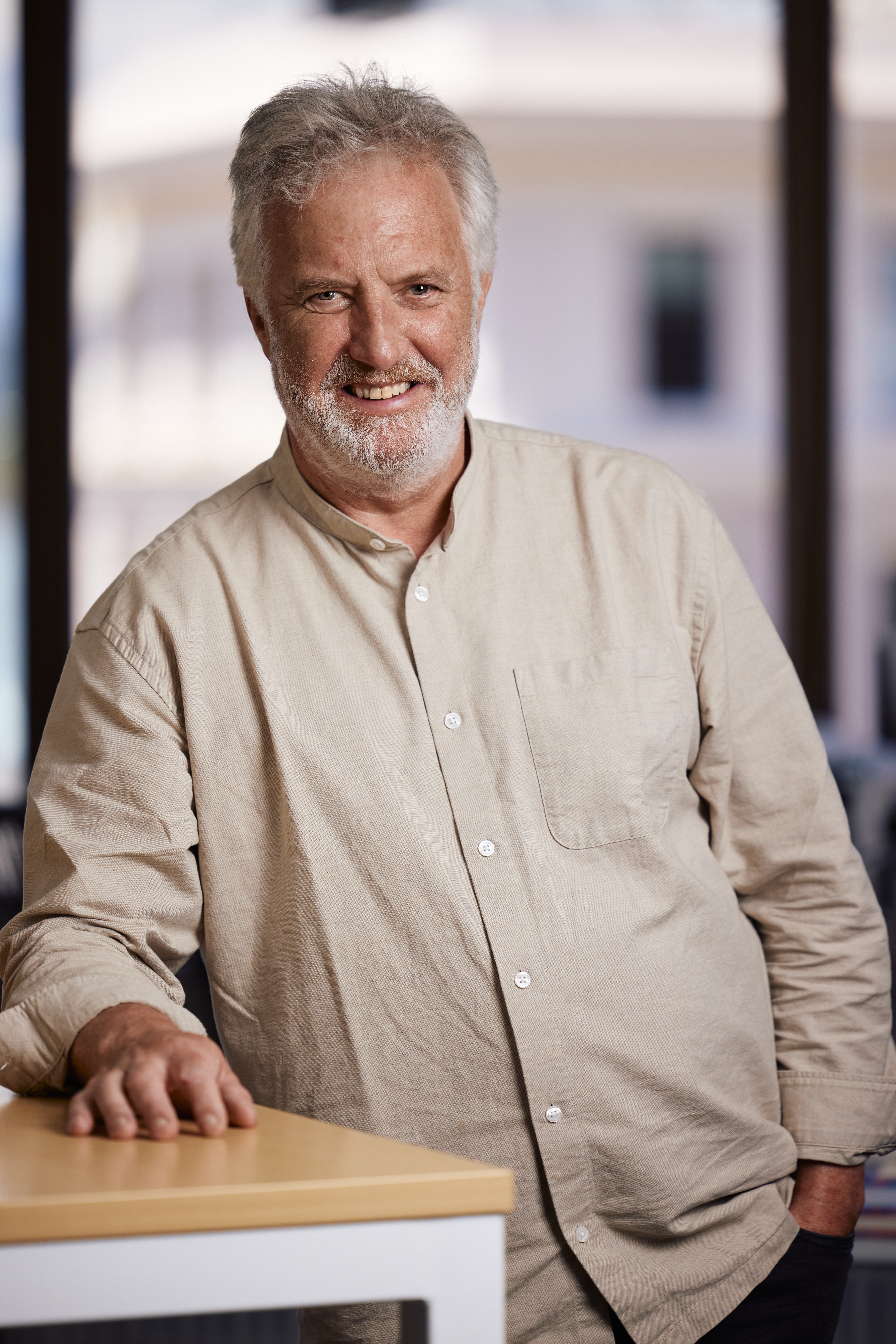 A head-shoulders-torso portrait of Jim Scully, facing the camera and smiling, with his right arm resting on a desk next to him.